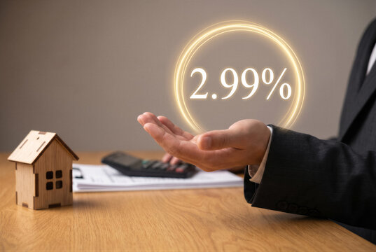 Businessman holding a glowing 299 percent interest rate symbol above his hand with a small wooden house model on a desk