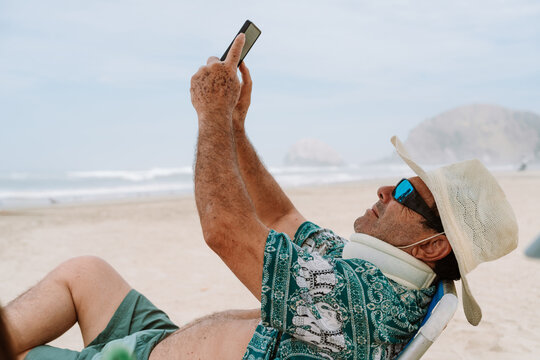mature Man with cervical collar Using Smartphone on Beach Chair 