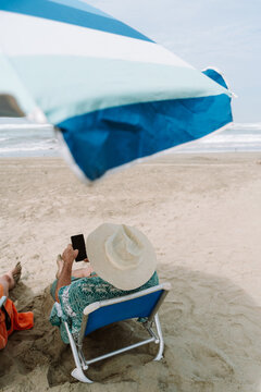 man Using Smartphone on Beach Chair Under Umbrella
