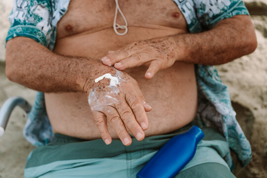 Mature Man Applying Sunscreen on Hand at Beach 