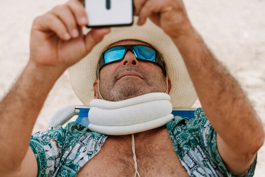 mature Man with cervical collar Using Smartphone on Beach Chair 