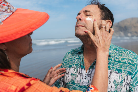 
Woman Applying Sunscreen on Man's Face at Beach on Sunny Day