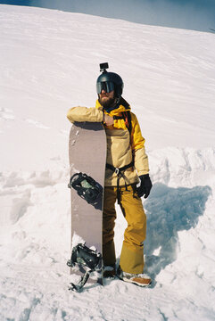 Man stands leaning on a snowboard