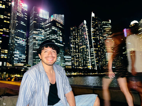 Man sitting by waterfront with city skyline at night in Singapore