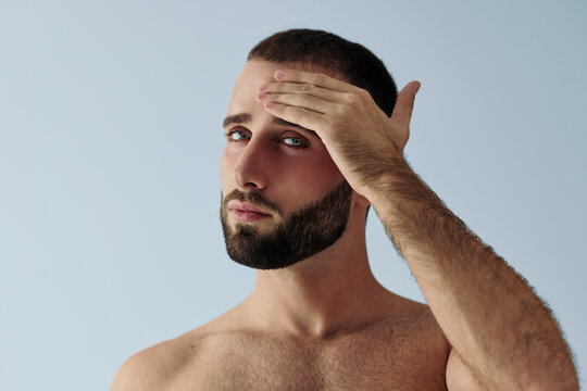 Man Poses With Hand on Forehead Against a Blue Background