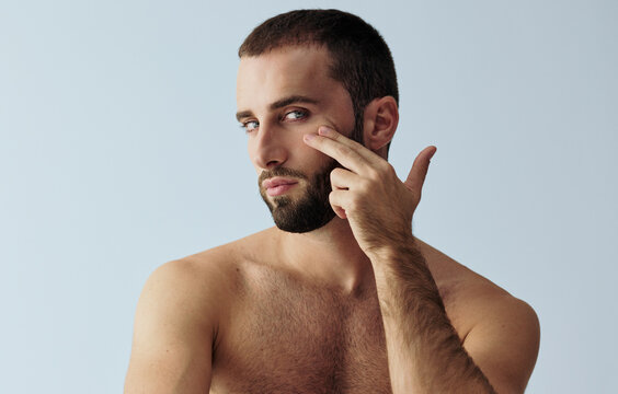 Man Points at Cheek While Posing Against a Blue Background