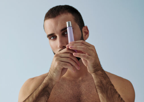 Model Holds Perfume Bottle in Front of Face in Light Setting