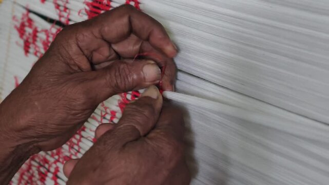 Close-up of artisan hands meticulously tying bundles of threads with plastic/raffia to create intricate patterns for traditional ikat weaving