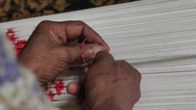 Close-up of artisan hands meticulously tying bundles of threads with plastic/raffia to create intricate patterns for traditional ikat weaving