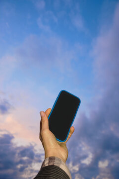 Hand holding smartphone against cloudy sky