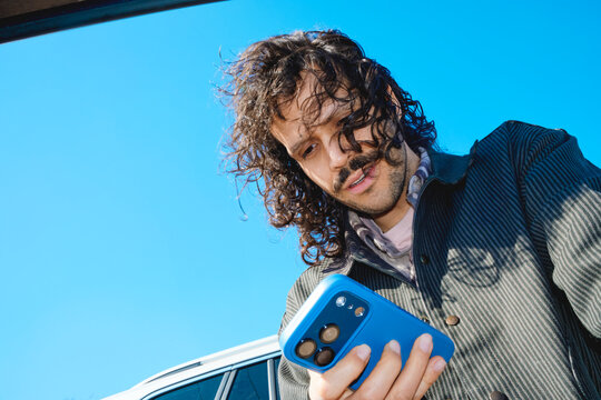 Man looking at smartphone beside parked car outdoors