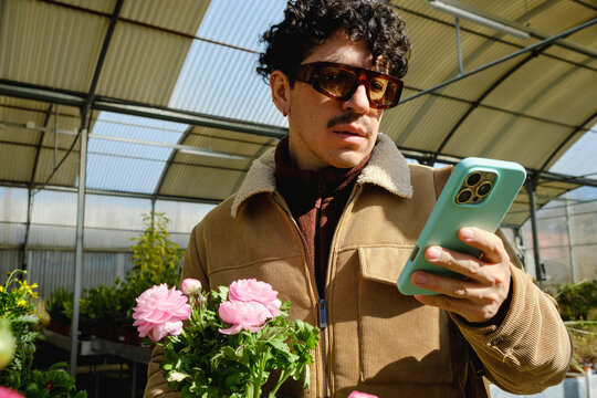 Man holding flowers while checking smartphone in greenhouse