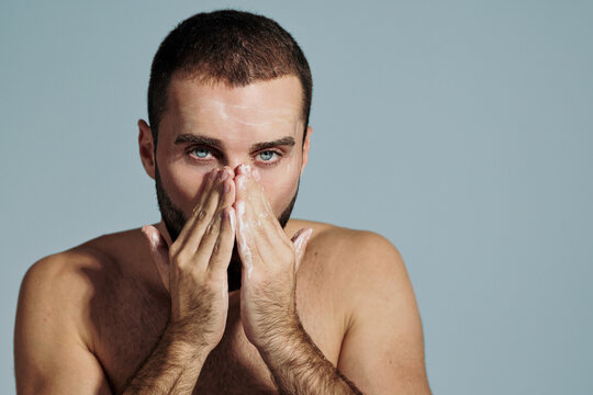 Man Washing Face With Cleanser in Front of Light Background