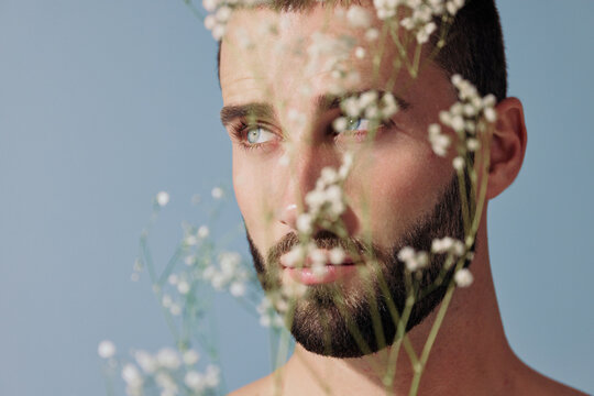 Man With Beard Poses in Front of Blue Background With Flowers