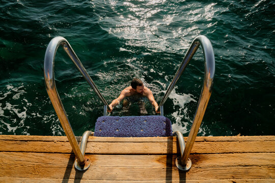Young man standing at the bottom of the ladder on a deck by sea