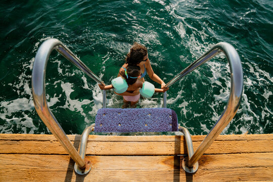 Girl and mom standing at the bottom of the ladder on a deck by sea