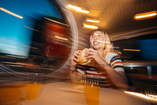 Young woman eating burger while traveling at night