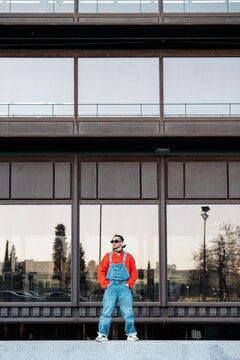 Young man standing outdoors wearing overalls and red shirt