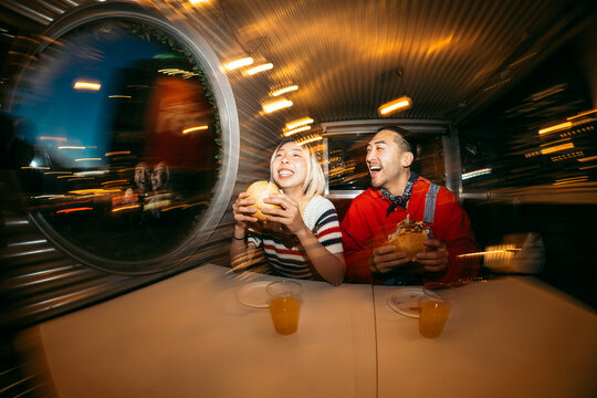 Cheerful young couple eating burgers at night diner