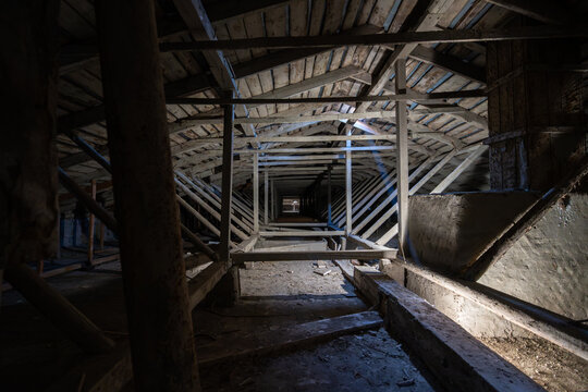 Attic wooden roof structure with beams and dramatic light, abandoned loft interior for architecture, renovation, heritage, mystery, construction inspection.