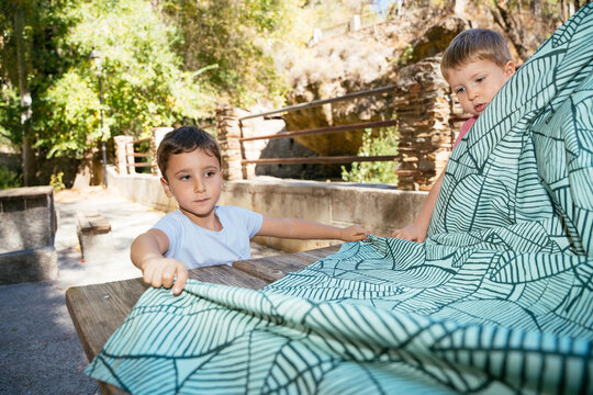 Children placing tablecloth on picnic table for outdoor picnic