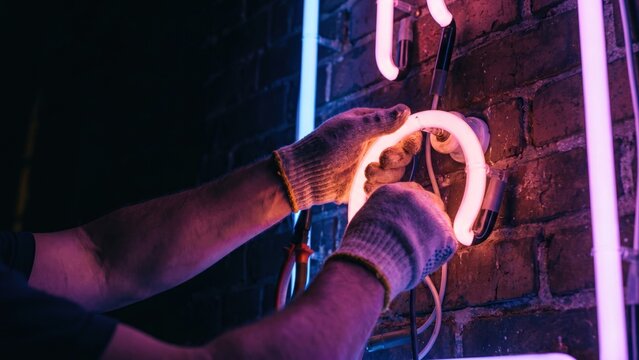 Hands Carefully Mounting Fragile Neon Glass Tubes into High Voltage Clips on a Wall