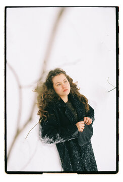Film Portrait of a Woman in Black Coat with Wind-Blown Hair in Snow