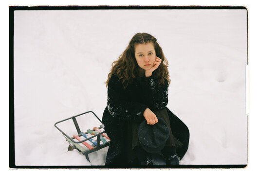 Film Portrait of a Woman Sitting on Snow with Vintage Sled