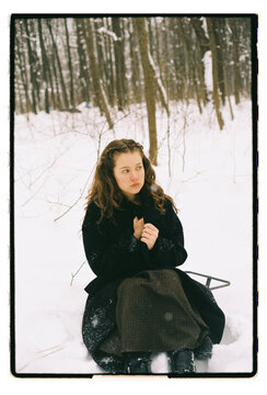 Film Portrait of a Young Woman Sitting on Sled in Snowy Forest