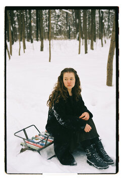 Film Portrait of a Young Woman Sitting on Sled in Snowy Forest