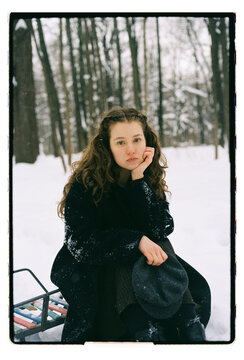 Film Portrait of a Young Woman Sitting on Sled in Snowy Forest