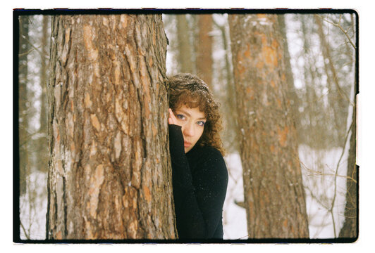 Film Portrait of a Woman Peeking Between Pine Trees in Winter Forest
