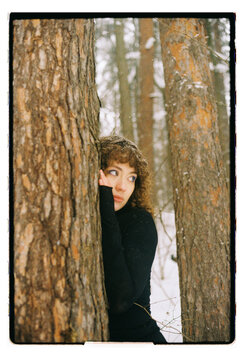 Film Portrait of a Woman Peeking Between Pine Trees in Winter Forest