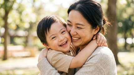 Fototapeta premium Smiling Asian mother and her young son with Down syndrome hugging in a park, inclusive family life and outdoor joy.