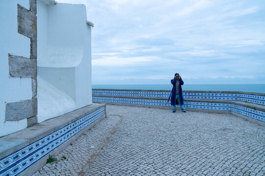 A blue woman standing by an old church by the sea