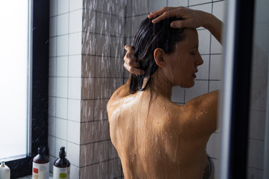 Woman Showering Under Rain Shower In Modern Bathroom