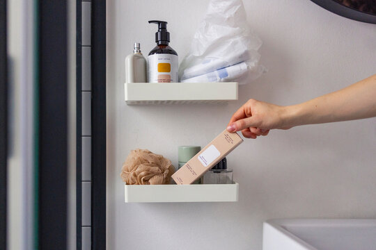 Hand Reaching for Skincare Product on Bathroom Shelf