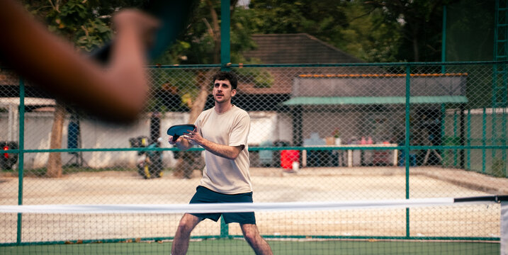 Young man playing pickleball on outdoor court, ready to hit the ball