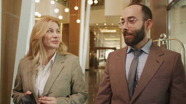 Male entrepreneur and his female colleague walking together through upscale hotel lobby, having conversation during business trip