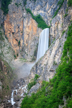 Aerial view of Boka Waterfall cascading down steep limestone cliffs surrounded by lush green forest in Slovenia.