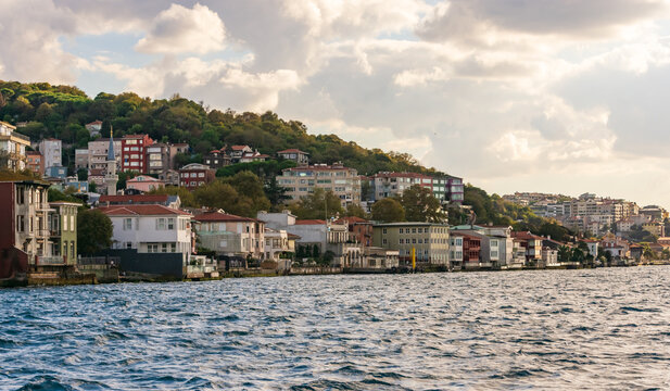 Vista panor&aacute;mica de la costa del B&oacute;sforo en Estambul, con casas otomanas tradicionales y apartamentos modernos enclavados en una exuberante colina verde bajo un cielo nublado al atardecer.
