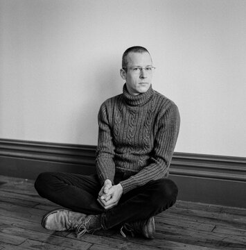 Portrait of a man sitting on a wooden floor.