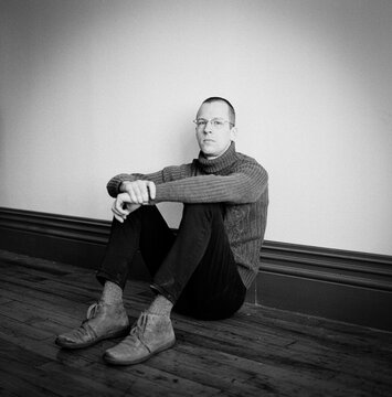 Portrait of a man sitting on a wooden floor.