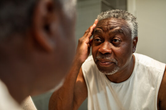 Senior man checking his face in bathroom mirror