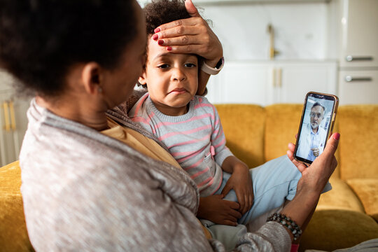 Mother comforting sick child during telehealth video call at home