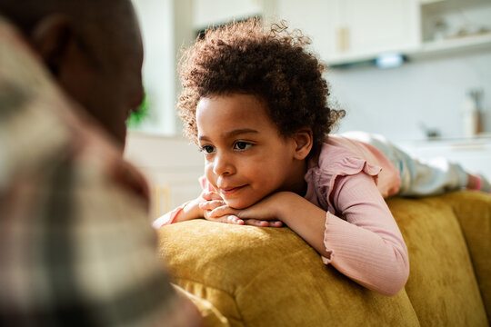Curly-haired girl listening to parent on sofa at home
