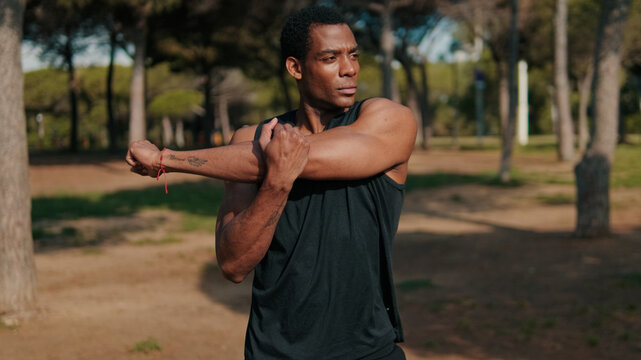 Athletic Man Stretches Arm Outdoors in Park
