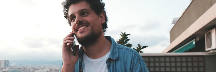 Obraz premium Close-up of young man talking on a mobile phone, in the background on the terrace his friends. Panoramic