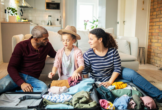 Parents and daughter packing suitcase for vacation at home