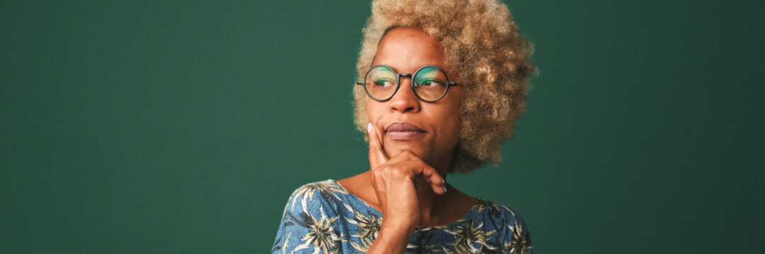 Pretty girl in glasses dressed in a blue t-shirt thinks about something tries to make a decision in mind isolated on green-blue background. Panoramic